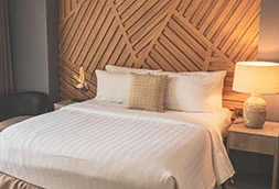 A neatly made bed in a bedroom with warm lighting and wooden wall decor.